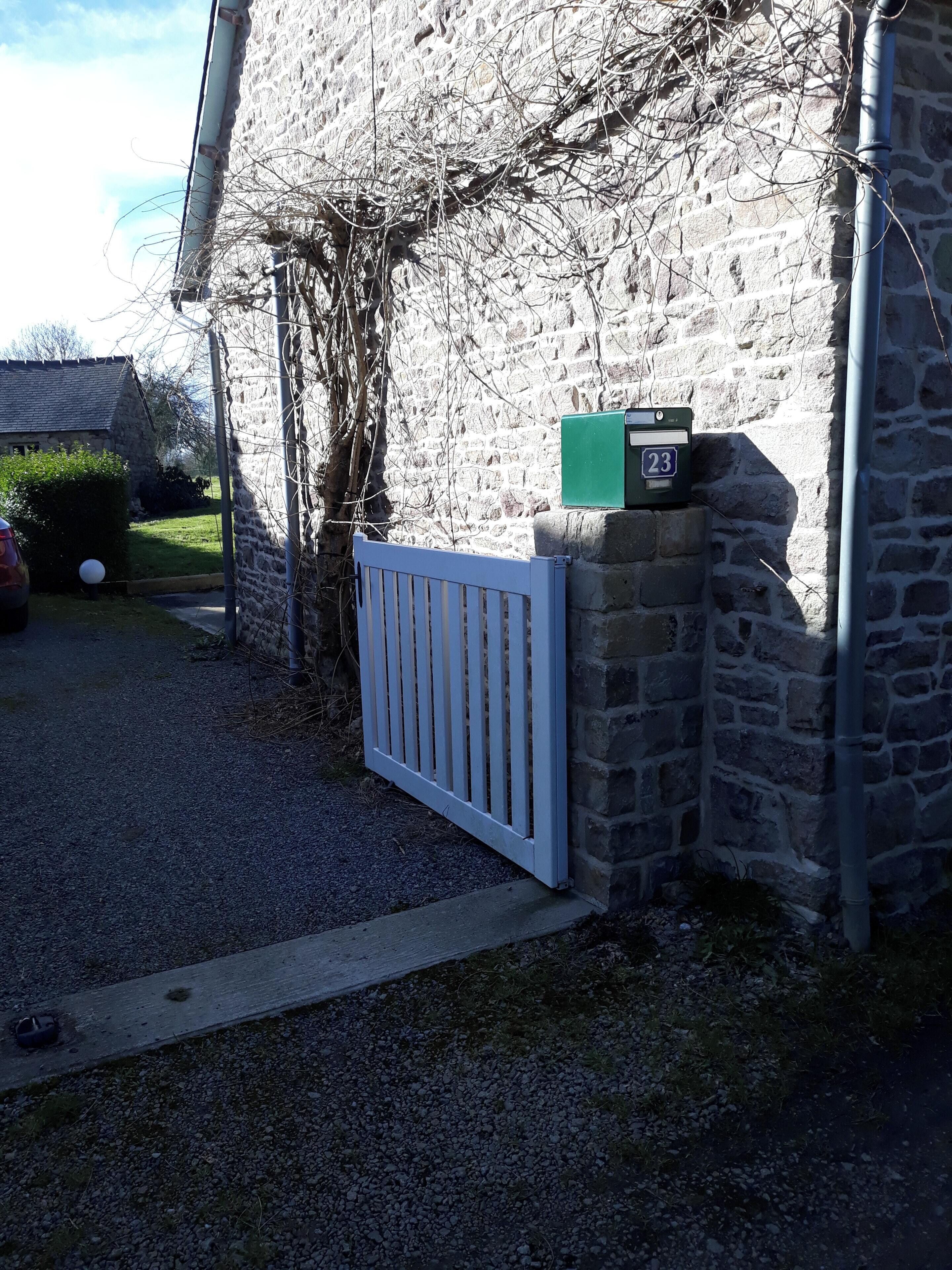 A stone building with a white gate, a mailbox, and a green box on the wall.