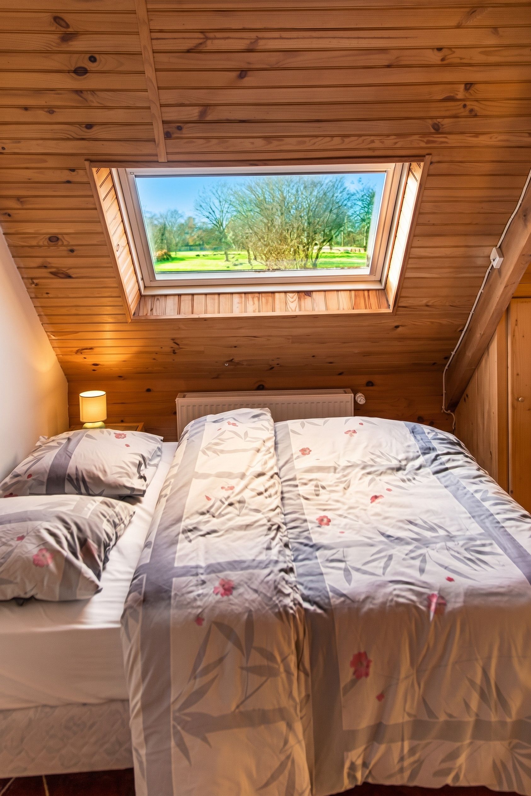 Een slaapkamer met dakraam, een bed met bloemenbedrukking en uitzicht op een park.