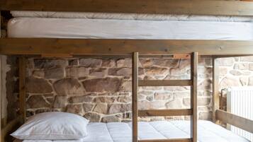 A bunk bed with white bedding in a room with stone walls and wooden beams.