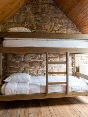 A bunk bed with white bedding in a room with stone walls and wooden beams.