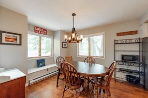 A dining area with a wooden table and chairs, a chandelier, and a view of the outdoors through large windows.