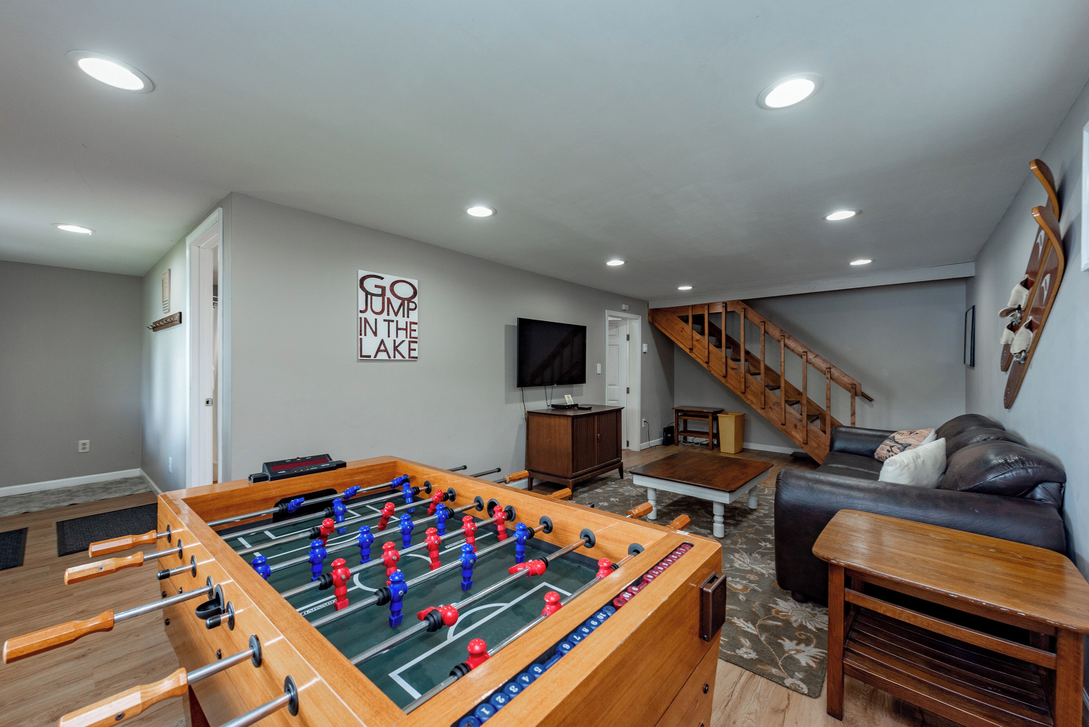 Una sala de estar con una mesa de fútbol de mesa, un sofá, un televisor y una escalera.
