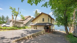 Une maison à deux étages avec un porche à l’avant, une allée en gravier et une terrasse en bois.