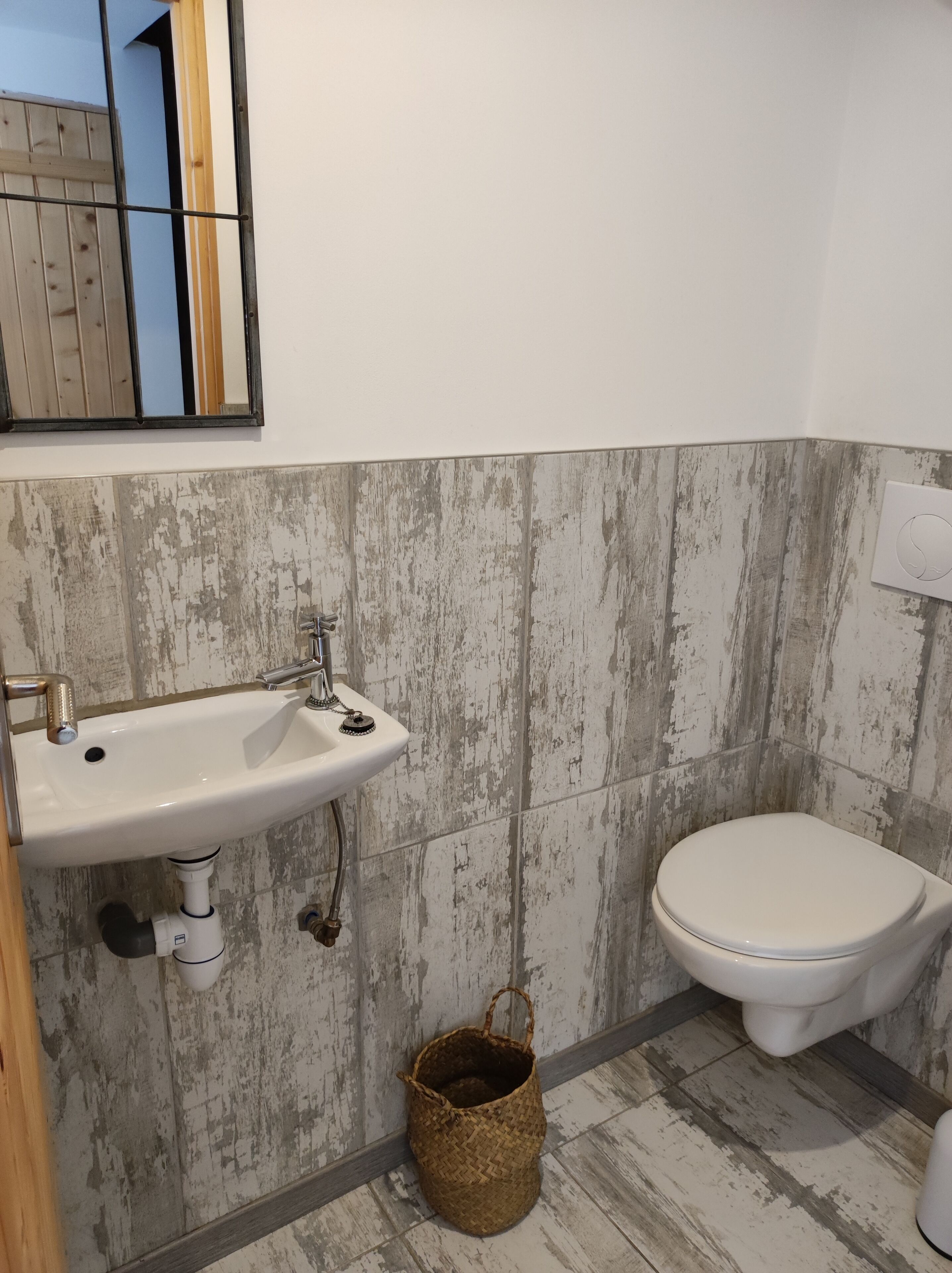 Ein Badezimmer mit einem weißen Waschbecken, einer Toilette und einem Holzkorb auf dem Boden.