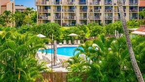 A hotel with multiple balconies, a swimming pool, and lush tropical vegetation.