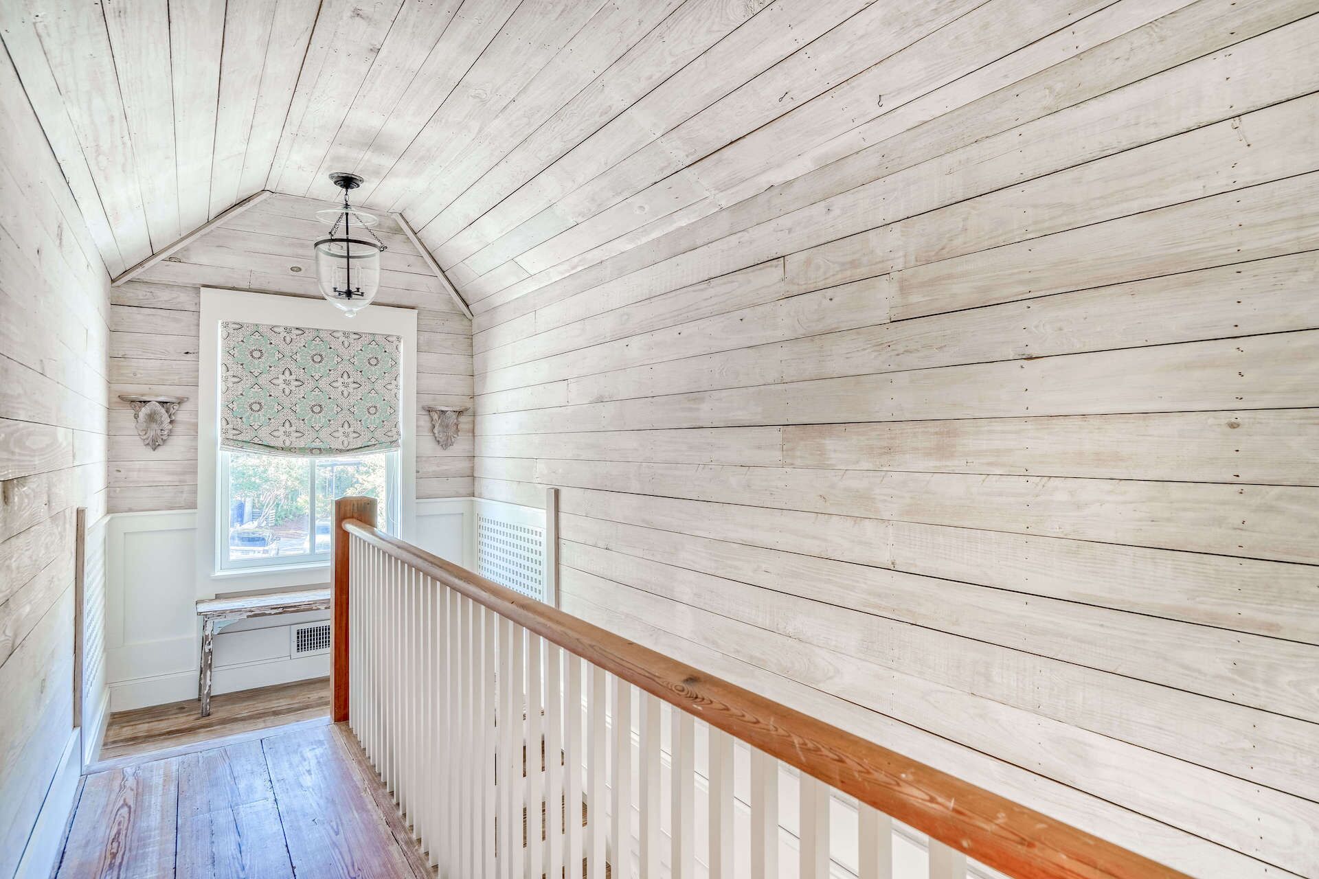 Un interior de madera con techo inclinado, una ventana con cortinas estampadas y una barandilla de madera.