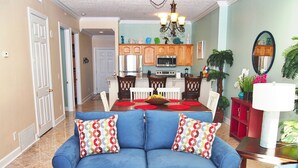 Ein Wohnzimmer mit einem blauen Sofa, einem Esstisch mit Stühlen und einer Küche im Hintergrund.