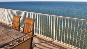 Ein Balkon mit Tisch und zwei Korbstühlen, mit Blick auf ein ruhiges Meer.