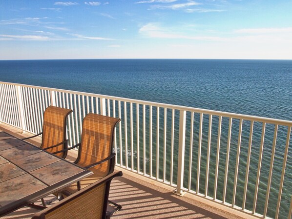 Un balcón con una mesa y dos sillas de mimbre, con vista al mar tranquilo.