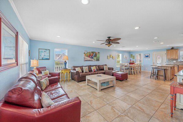 A spacious living room with a brown leather sofa, a wooden coffee table, and a ceiling fan. - 6 Bedroom/4 Bath Very close to the beach and to town! 2nd floor Deck seating wi (Port Aransas)