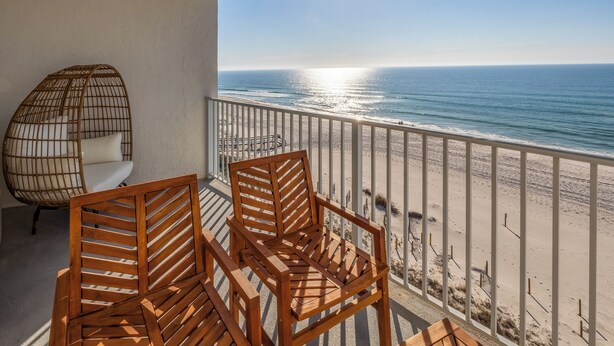 A balcony with wooden chairs and a wicker chair overlooking a beach. - Beachfront Beauty - Practically New 1BR Condo! Gulf Front At Perdido Skye (Pensacola)