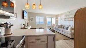 A modern kitchen with a large island, pendant lights, and a dining area with a sofa and chairs. - Beachfront Beauty - Practically New 1BR Condo! Gulf Front At Perdido Skye (Pensacola)