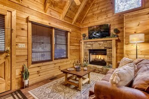 L’intérieur d’un chalet confortable, avec une cheminée en pierre, des murs en bois, un canapé confortable et une petite table agrémentée d’objets décoratifs.