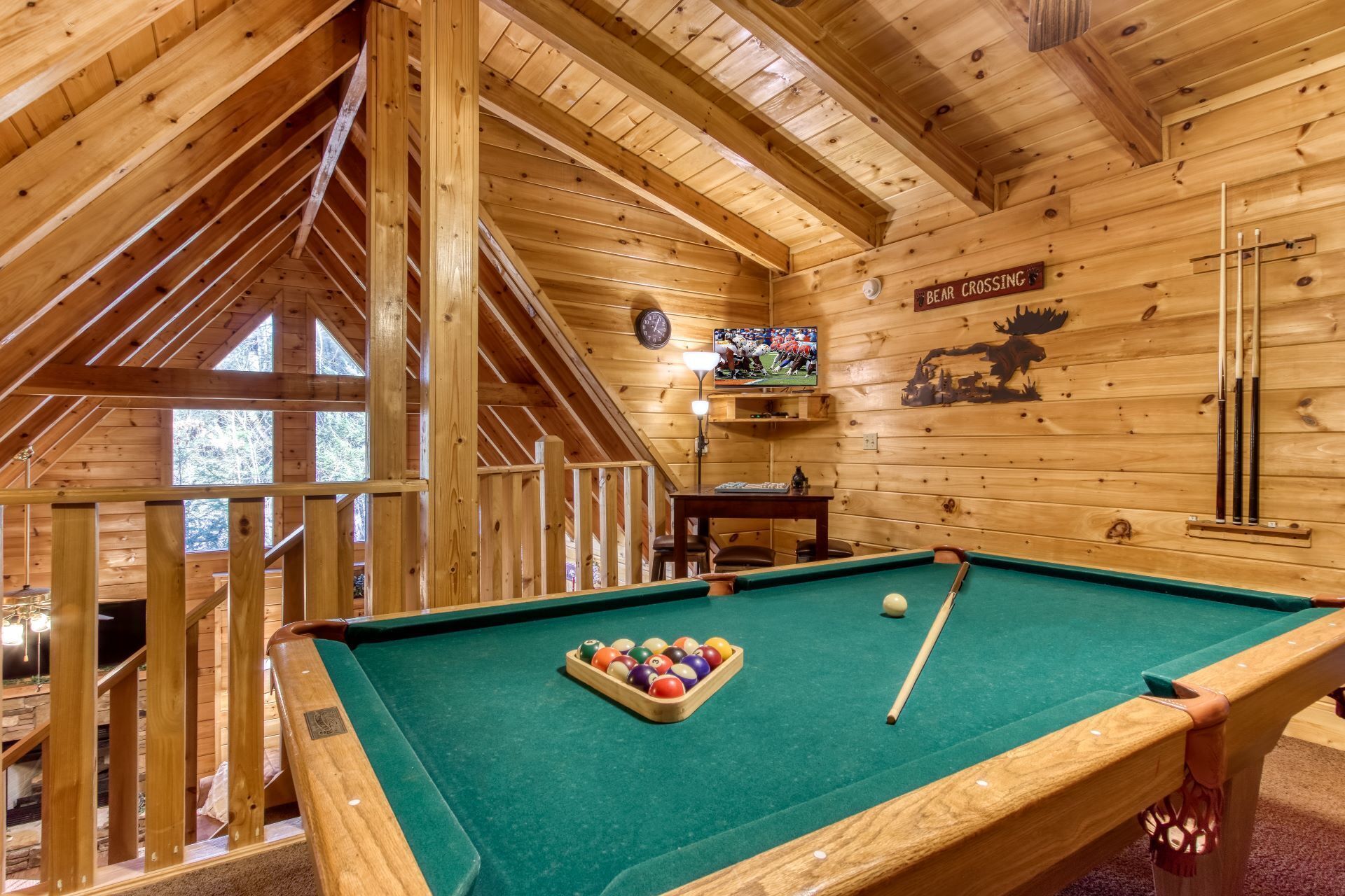 A wooden cabin interior with a pool table, a clock, and a bear crossing sign.