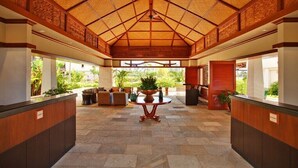 A spacious lobby with a high ceiling, a central round table, and a view of greenery outside. - Summer Sale Rates- 2BR/2BA on Sunset Side of BT (Kapolei)