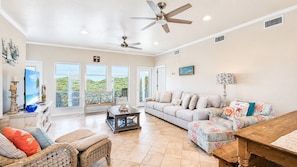 A spacious living room with a large window overlooking a scenic view, a ceiling fan, and a cozy seating area. - Just steps to beach access, this coastal home has everything you will need for y (Port Aransas)