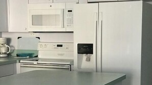 Cocina equipada con microondas, cafetera y dispensador de agua. Hay dos taburetes con asientos de mimbre.