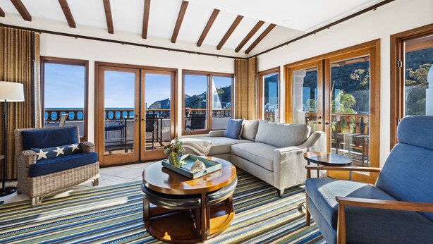 A spacious living area with a large window overlooking a scenic view, a comfortable sofa, a coffee table, and a wicker chair.