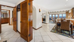A spacious dining area with a large table and chairs, a view of the ocean through large windows, and a modern kitchen in the background.
