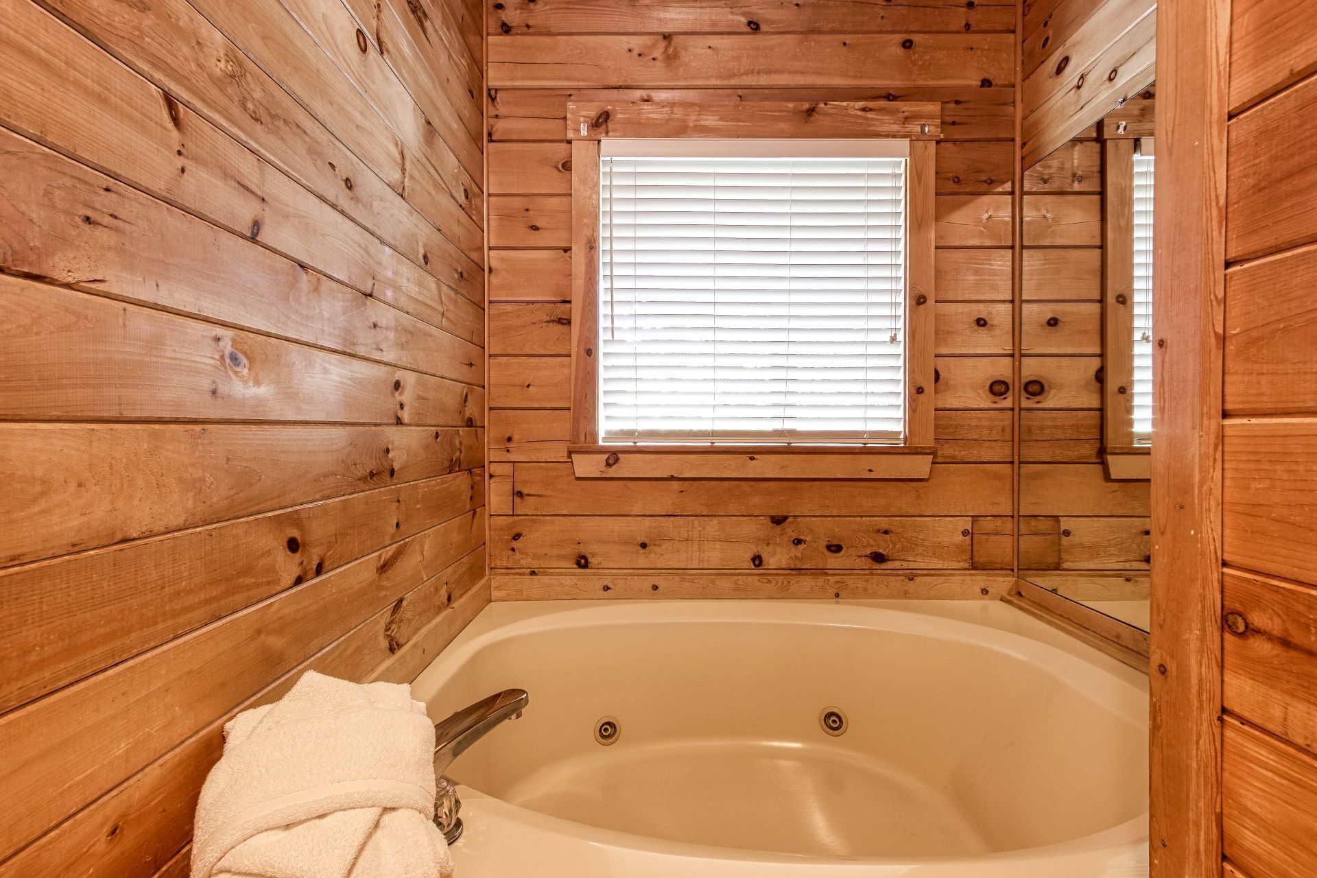 Ein Badezimmer einer Holzhütte mit einer Badewanne, einem Fenster mit Jalousien und einem Spiegel.