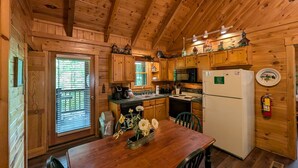 A wooden cabin kitchen with a wooden table, chairs, a refrigerator, a stove, and a microwave.