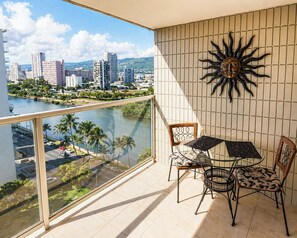 Un balcón con vista a la ciudad, una mesa con sillas y un muro decorativo con motivos solares.
