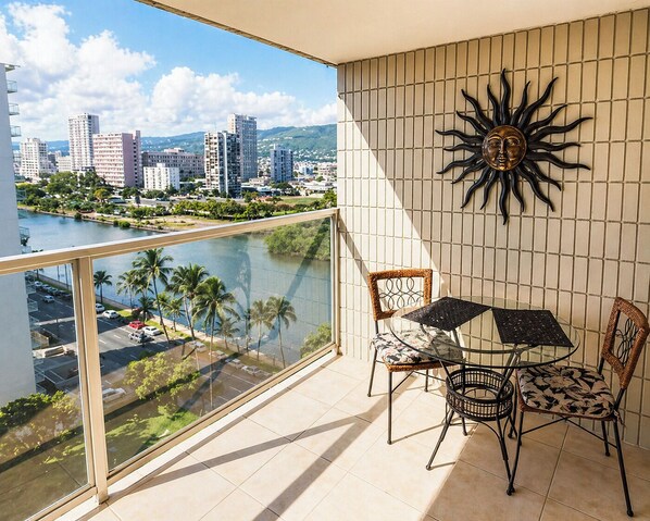 Un balcón con vista a la ciudad, una mesa con sillas y un muro decorativo con motivos solares.