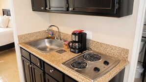 A compact kitchen with a sink, two stovetops, a coffee maker, and dark cabinetry. - Clean studio at the heart of Waikiki!! (Honolulu)