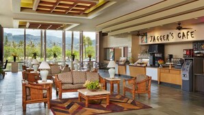 A spacious lobby with a seating area featuring sofas and armchairs, a coffee bar named "Jagger's Cafe," and large windows offering a view of greenery and mountains. - Clean studio at the heart of Waikiki!! (Honolulu)