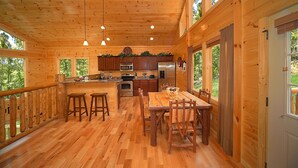 Una cabaña de madera con cocina, comedor y ventanas grandes.