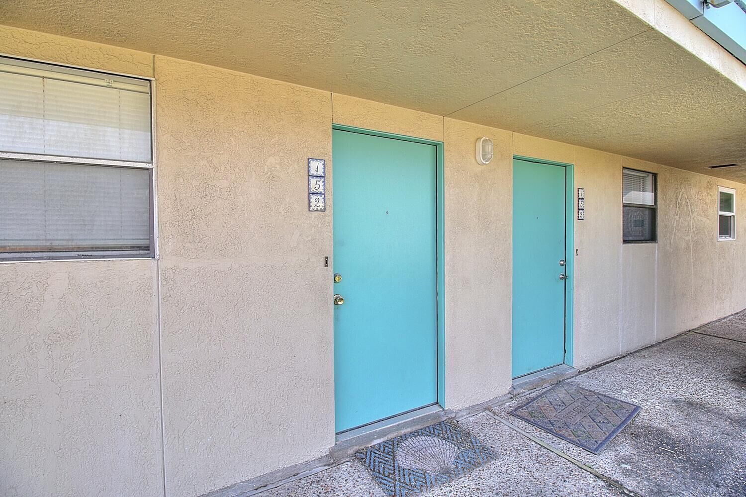 A row of three doors with numbered plaques, a small window, and a concrete floor with a metal grate.