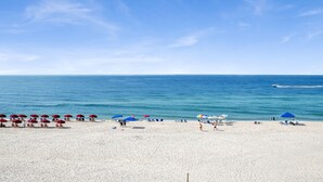Een strand met wit zand, helderblauw water en enkele parasols en strandstoelen.