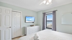 Een slaapkamer met een bed, een dressoir, een televisie en een raam met uitzicht op het strand.