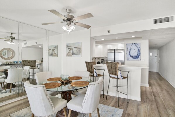 A modern kitchen with white cabinets, a stainless steel refrigerator, and a dining area with a glass table and white chairs.