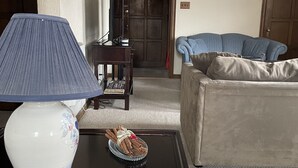 A living room with a blue lamp, a vase with a floral design, a plate with cinnamon sticks and berries, a red book, and a blue sofa.