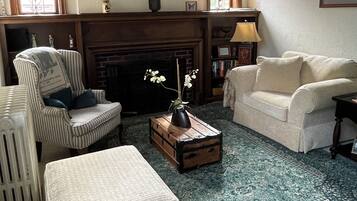 A living room with a large wall clock, a fireplace, striped armchair, and a patterned rug.
