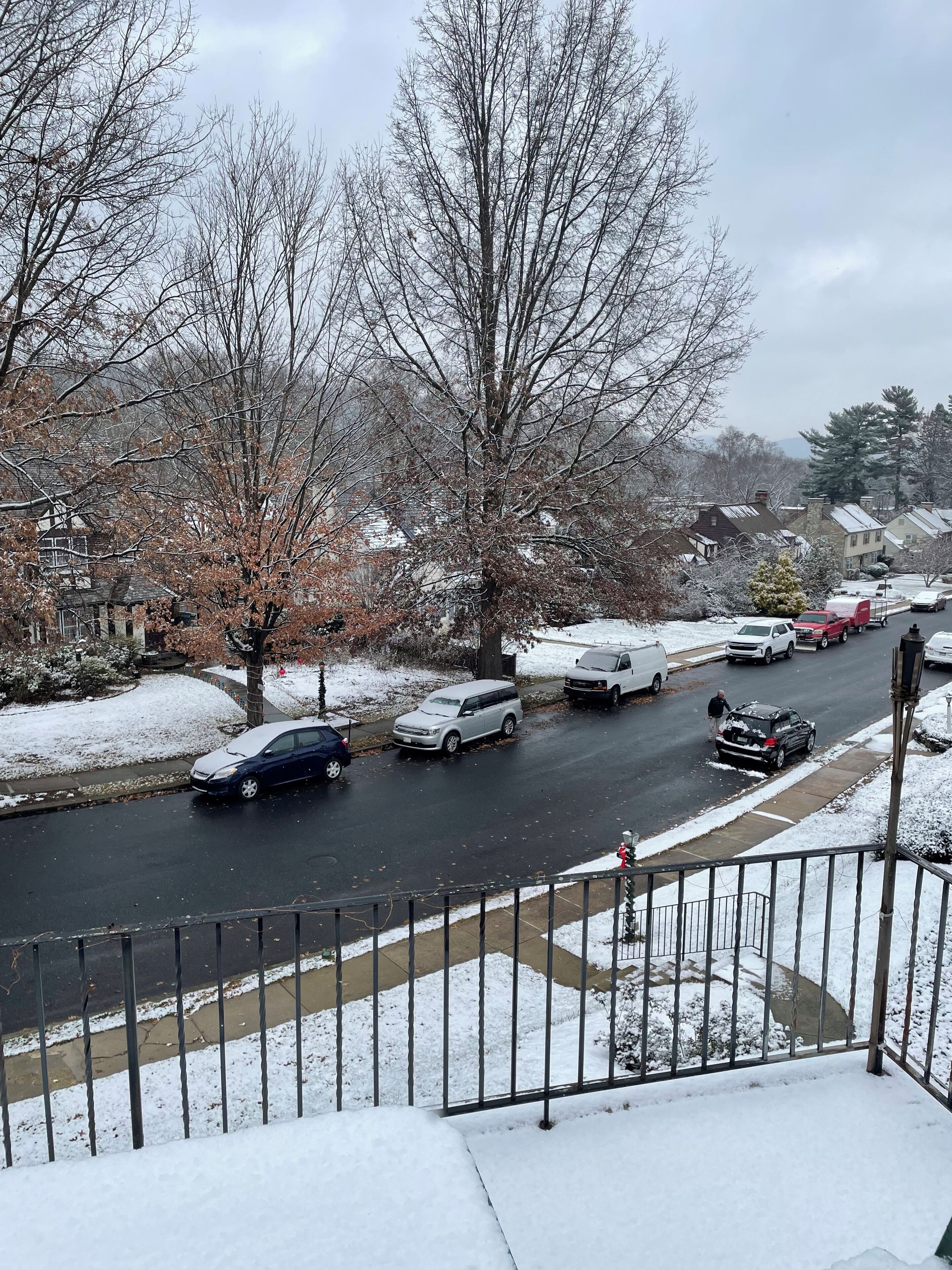 Una calle residencial con aceras cubiertas de nieve y coches aparcados.