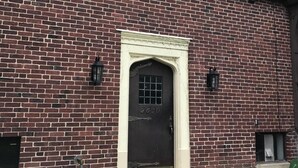 A brick building with a dark brown door, a small window, and a mailbox.
