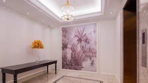 A hallway with a marble floor, a dark wooden bench, a vase of yellow flowers, and a large wall mural of tropical plants. - The Bamboo Hotel Hong Qiao Airport (Shanghai)