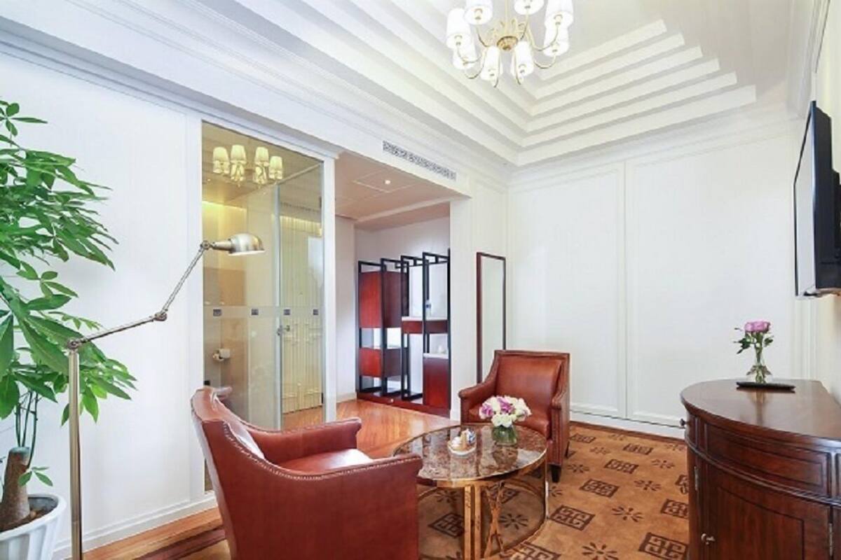 Ein Hotelzimmer mit einer großen Topfpflanze, einem runden Tisch mit einer Vase, einer Holzkabine und einem an der Wand montierten Fernseher.