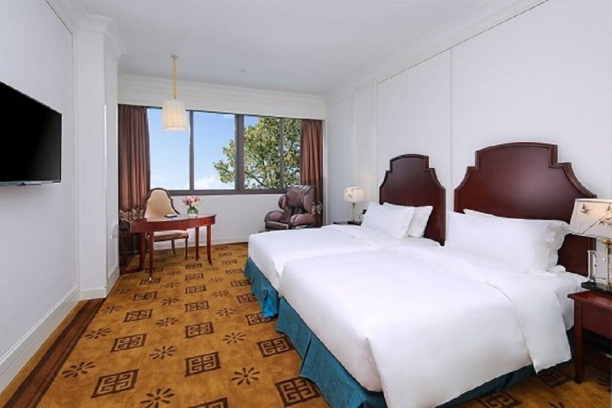 Ein Hotelzimmer mit zwei Betten, einem Fernseher, einem Schreibtisch mit Stuhl und einem Fenster mit Vorhängen.