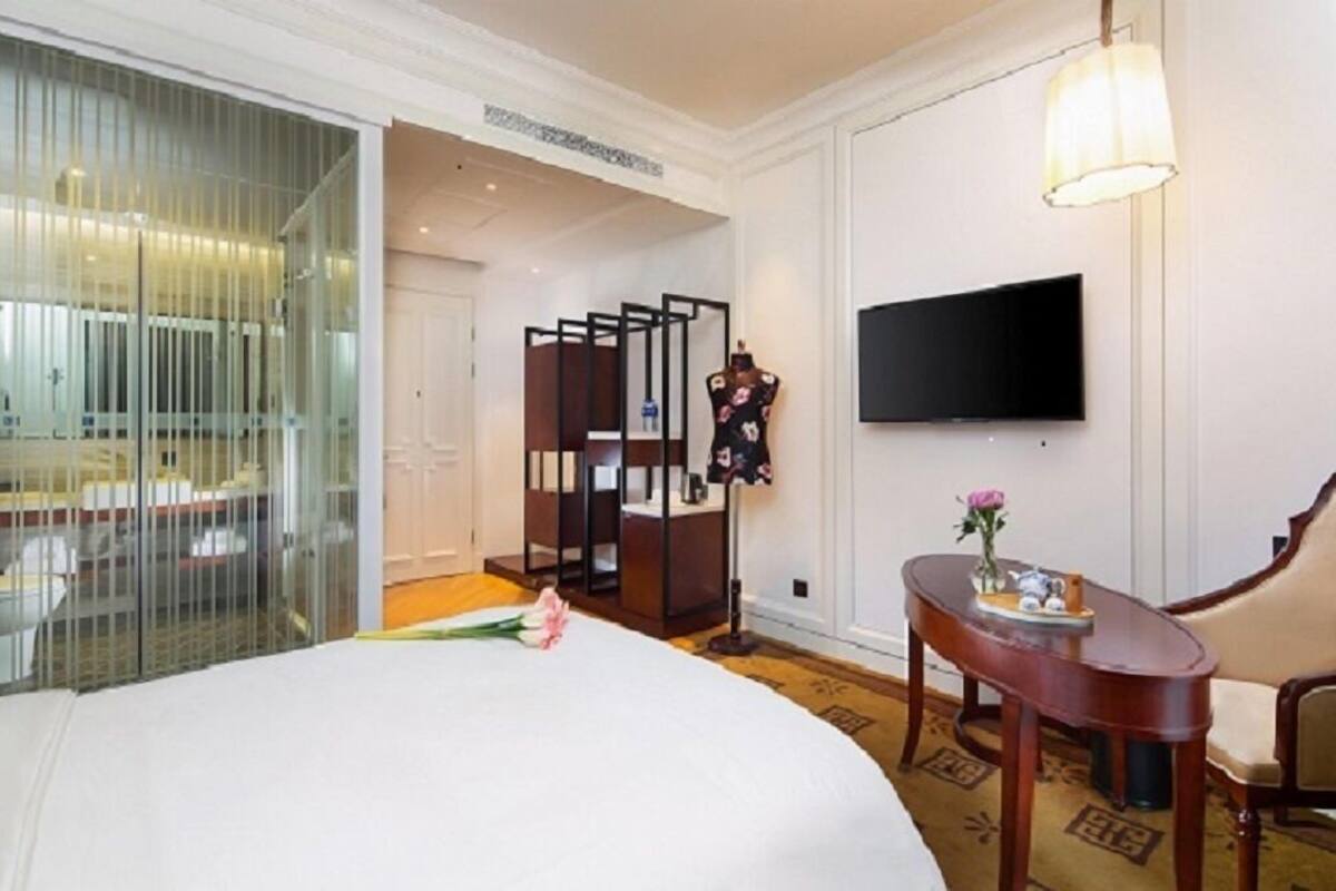 Ein Hotelzimmer mit einem großen Bett, einem an der Wand montierten Fernseher, einem Nachttisch aus Holz mit einer Vase und einem Sessel.