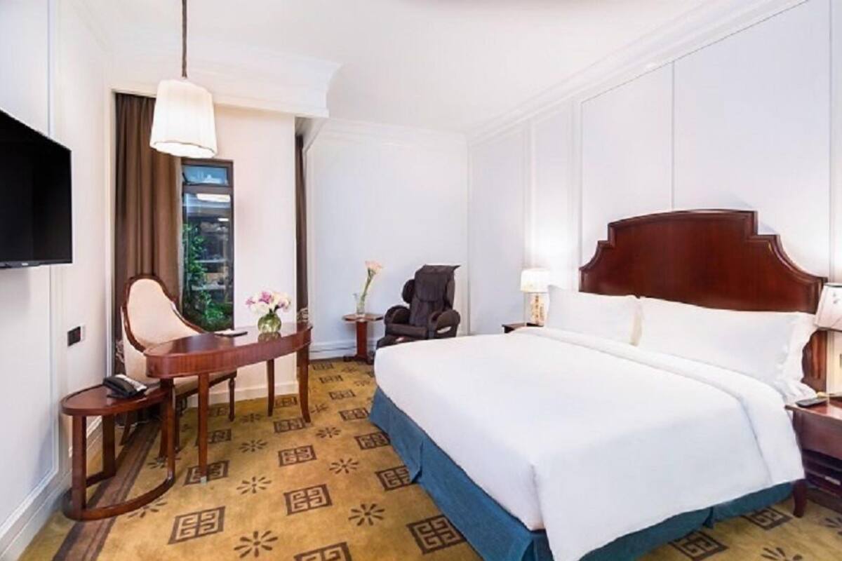 Ein Hotelzimmer mit einem großen Bett, einem Schreibtisch mit Stuhl, einem Fernseher und einem Fenster mit Vorhängen.