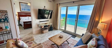 Sala de estar con sofá, mesa de centro, televisión y balcón con vista al océano.