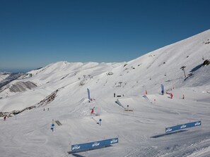 A snowy ski slope with ski lifts, flags, and a clear sky.