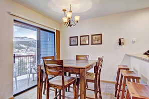 Uma sala de jantar com mesa e cadeiras de madeira, um candelabro e vista para montanhas através de uma grande porta de vidro deslizante.