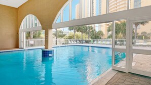 Una piscina interior con paredes de vidrio transparente y vistas a palmeras y edificios.