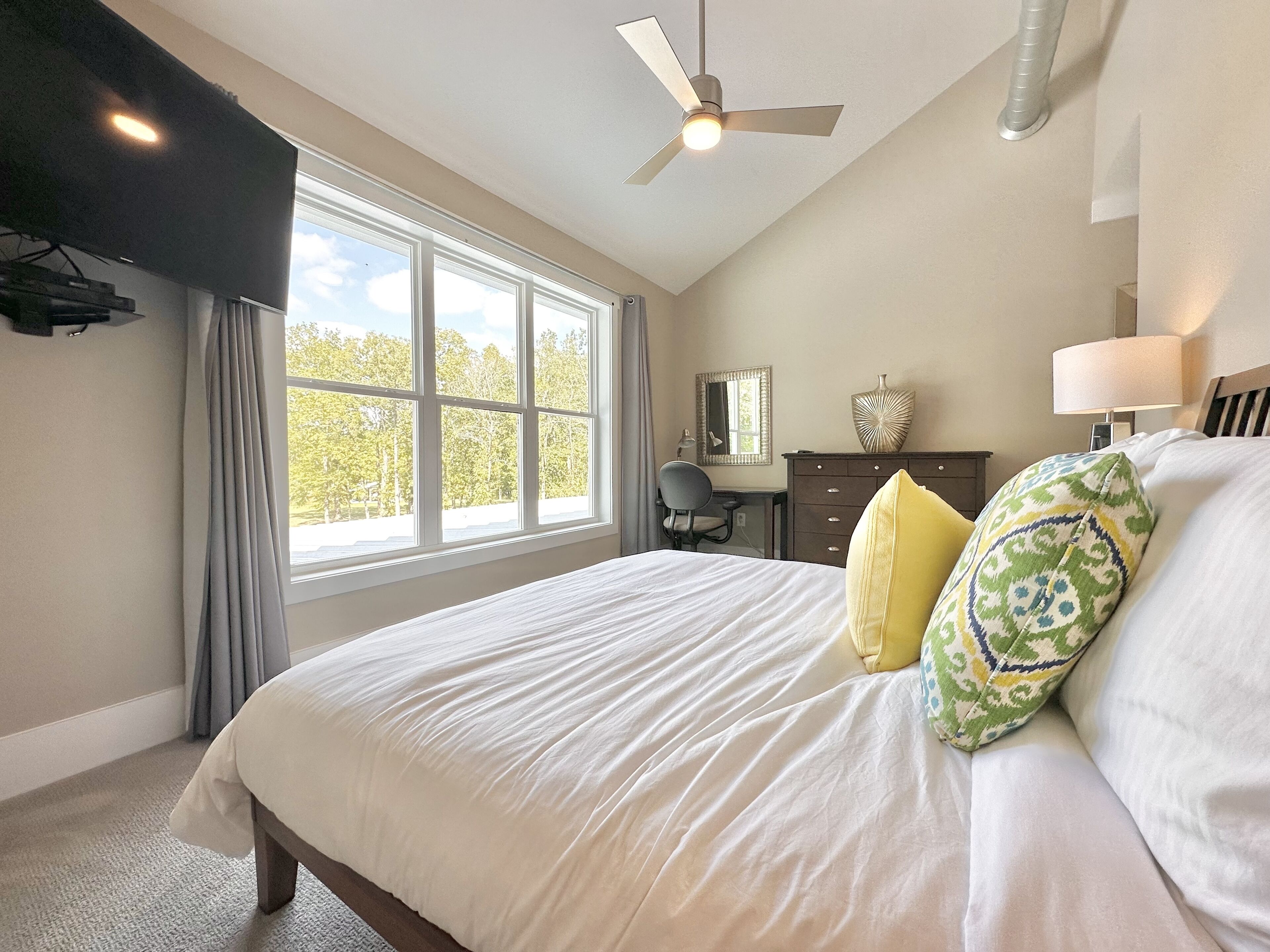 A bedroom with a large bed, a desk, a chair, and a ceiling fan.