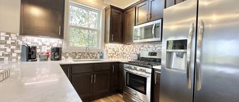 A modern kitchen with dark wood cabinets, stainless steel appliances, a large island, and a window providing natural light.