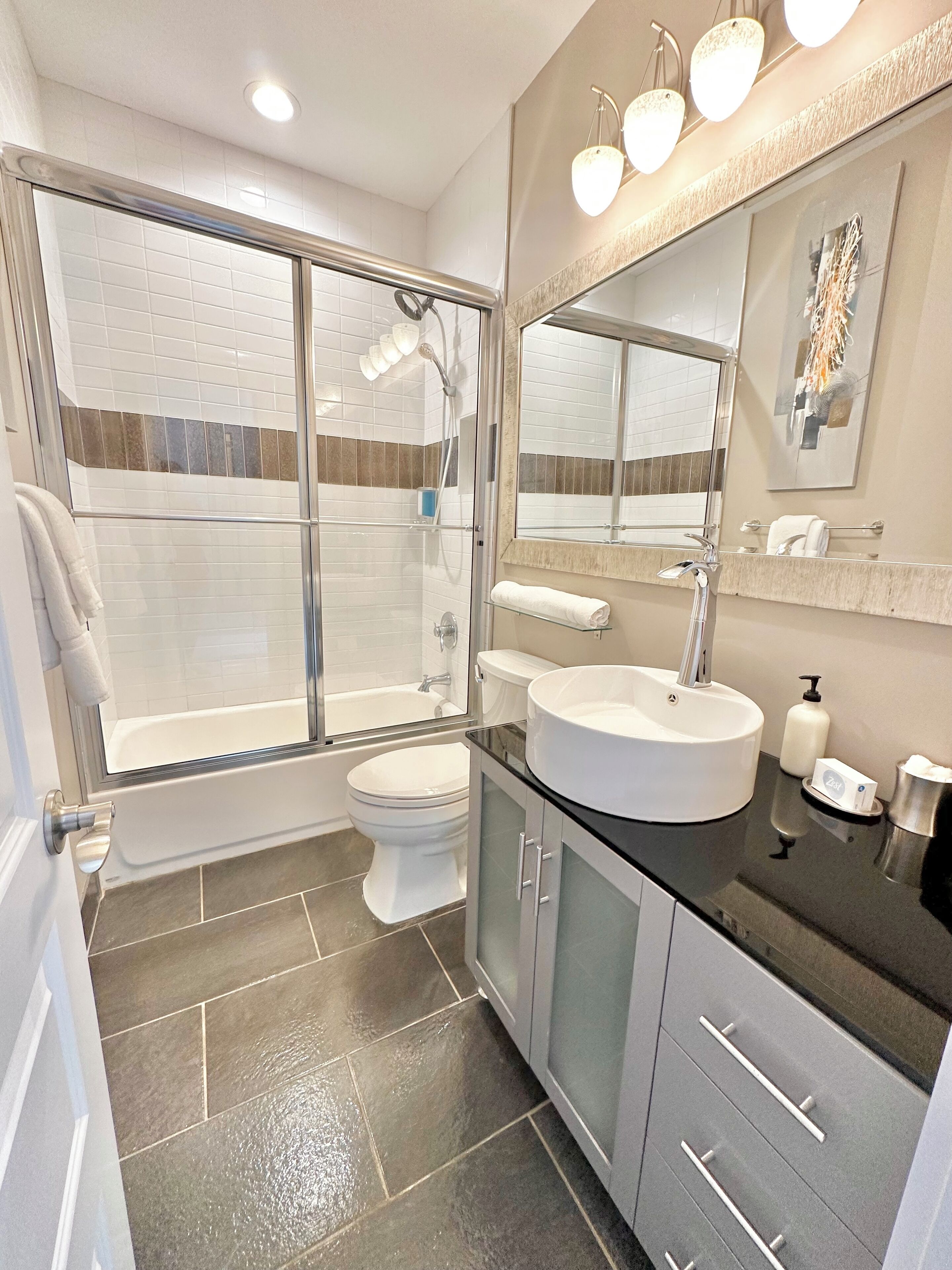 A modern bathroom with a glass-enclosed shower, a bathtub, a toilet, and a vanity with a sink and mirror.